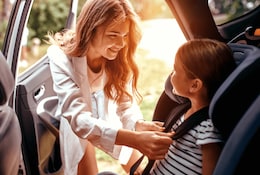 Mutter schnallt ihre Tochter in einem Autokindersitz an